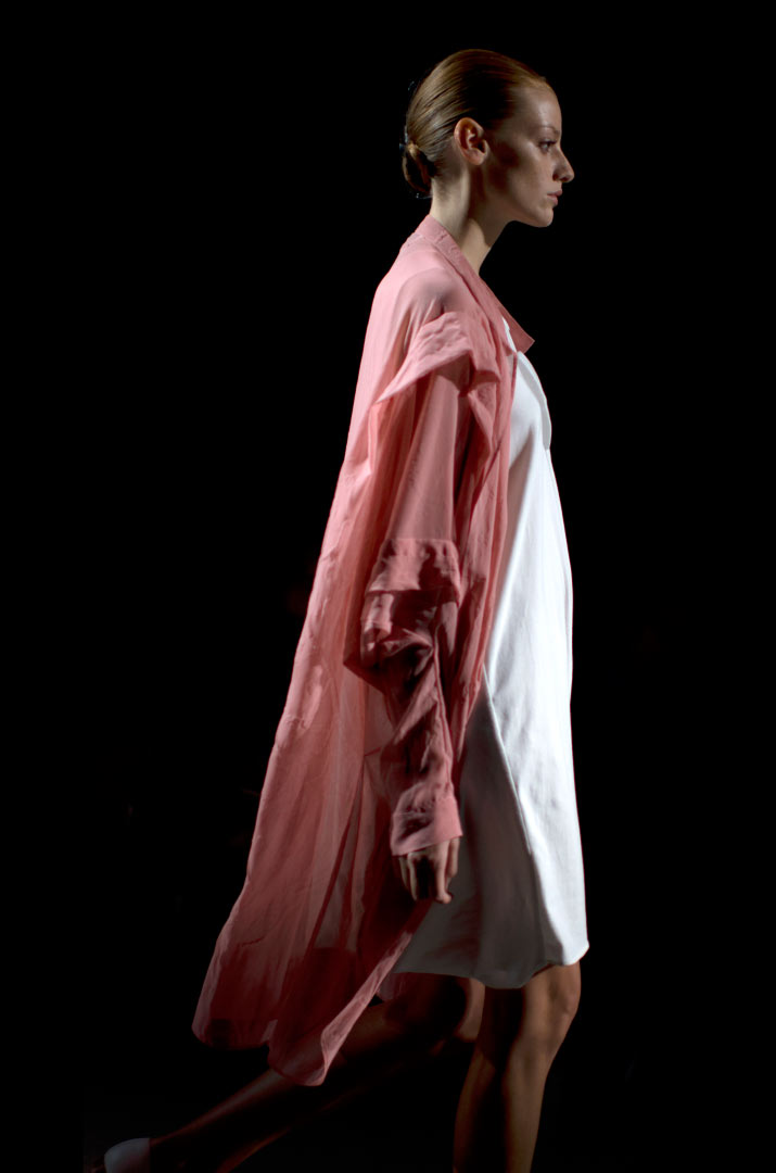 Anrealage Spring 2012 Fashion Artist Danny Roberts Photo of the profile of a model walking in a Soft Pink Overcoat with a white Anrealage dress in the Collection from Tokyo Fashion Week 2012